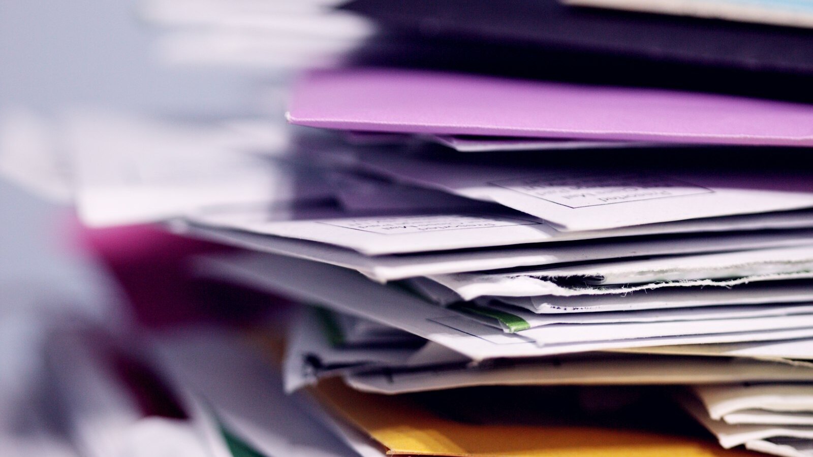 A tall untidy stack of reports and folders on an office desk