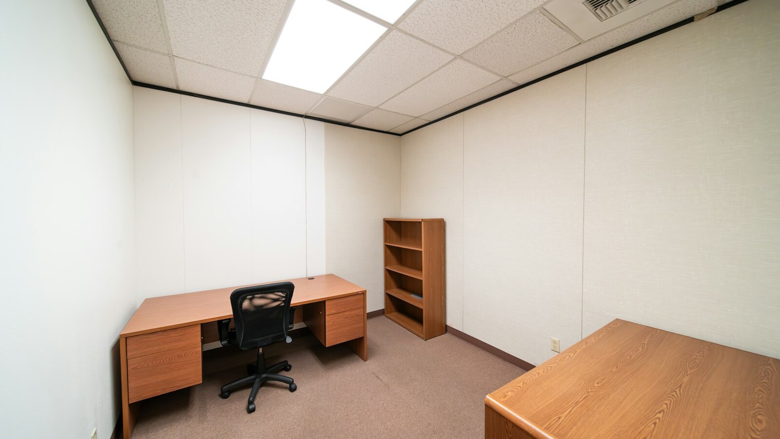 A nearly empty office with one desk, one chair and bare shelves