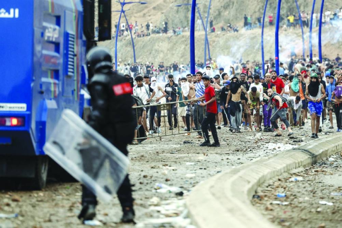 A crowd advances towards Moroccan riot police on a road strewn with stones near Fnideq