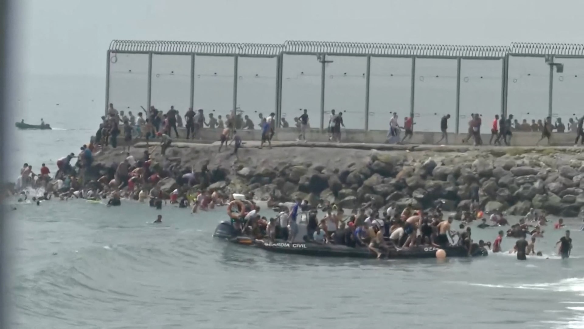 A Guardia Civil patrol boat is crowded and surrounded by swimmers at Ceuta's sea border