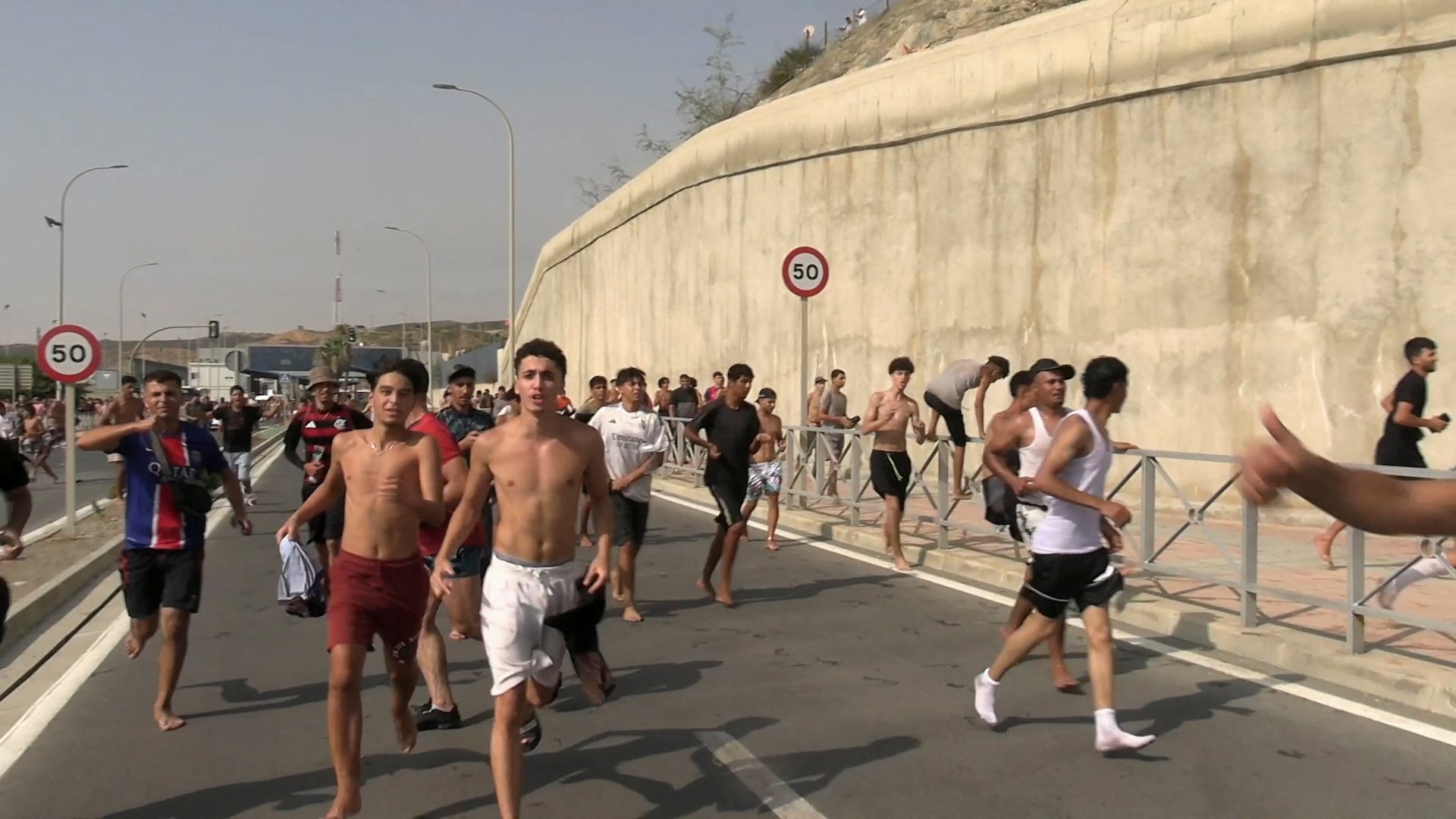 Young men run along a road inside Ceuta after crossing the breakwater from Morocco